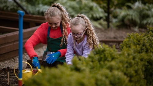 Two children gardening in a walled garden with small sized tools